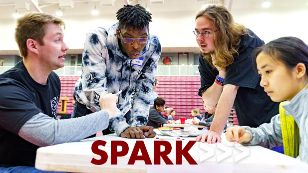 Image shows four students working on a SPARK project together at a table. 