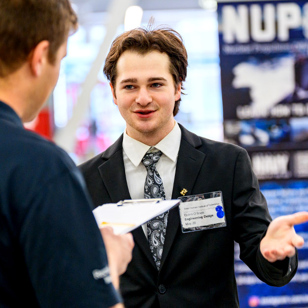 A student in professional attire smiles and shakes the hand of an employer. 