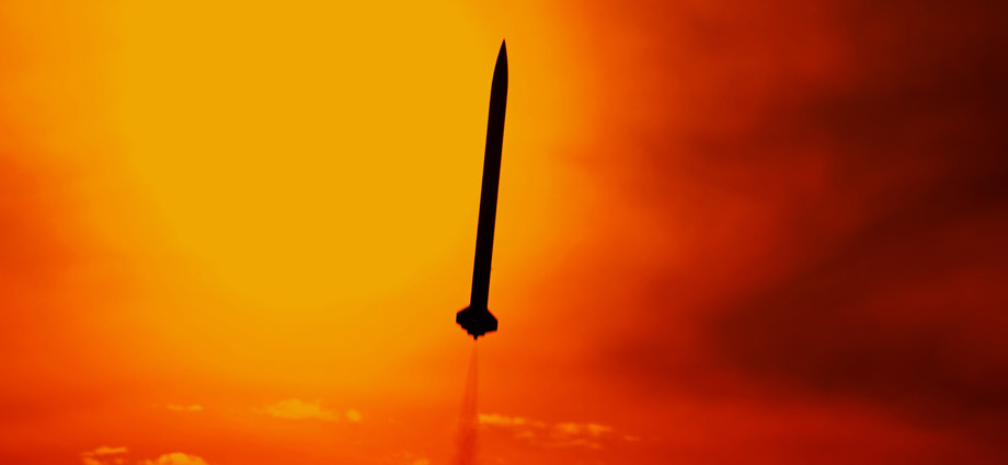 A rocket silhouetted against a fiery orange and yellow sunset.