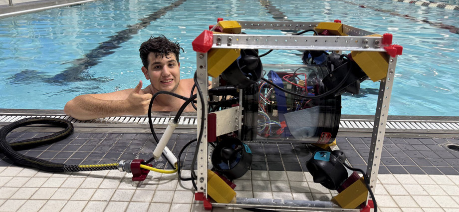A student gives a thumbs-up from a pool with the underwater robot.