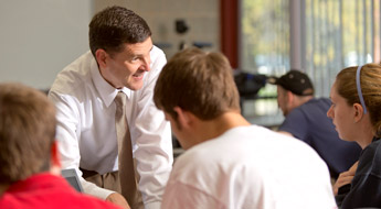 !Professor Rick Stamper smiling and working with students in a Rose-Hulman classroom.