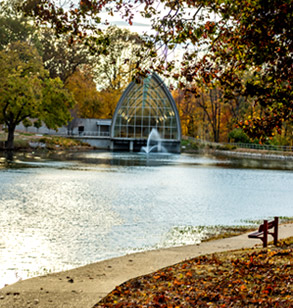 Image shows sunlight glistening on Speed Lake with fall colors in the trees and the fountain going in the lake in front of White Chapel.