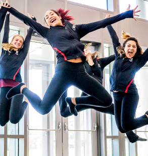 Four female members of the Rose-Hulman dance team leaping into the air and smiling in the lobby of Hatfield Hall.