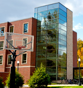 The glassed-in stairwell of Percopo Hall, a residence hall. A basketball goal is in the foreground